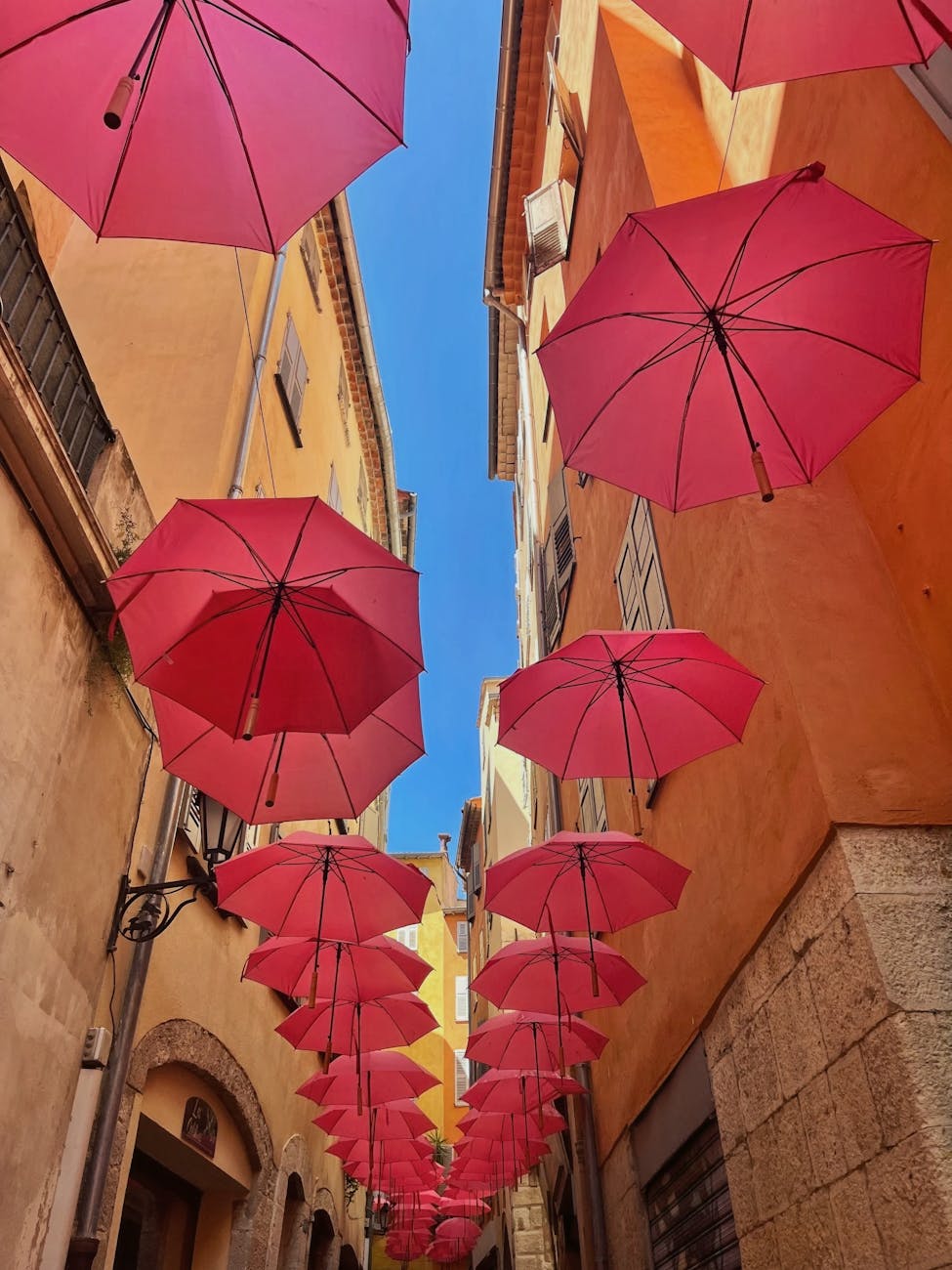 Parasols roses suspendus au-dessus d'une ruelle pavée à Grasse