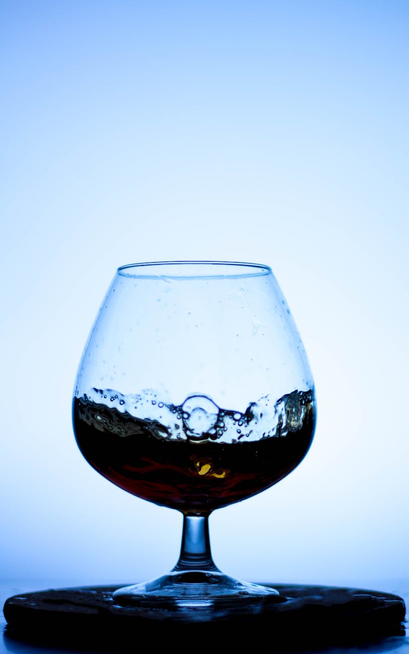 Verre de cognac ambré devant des fûts de chêne en chai charentais