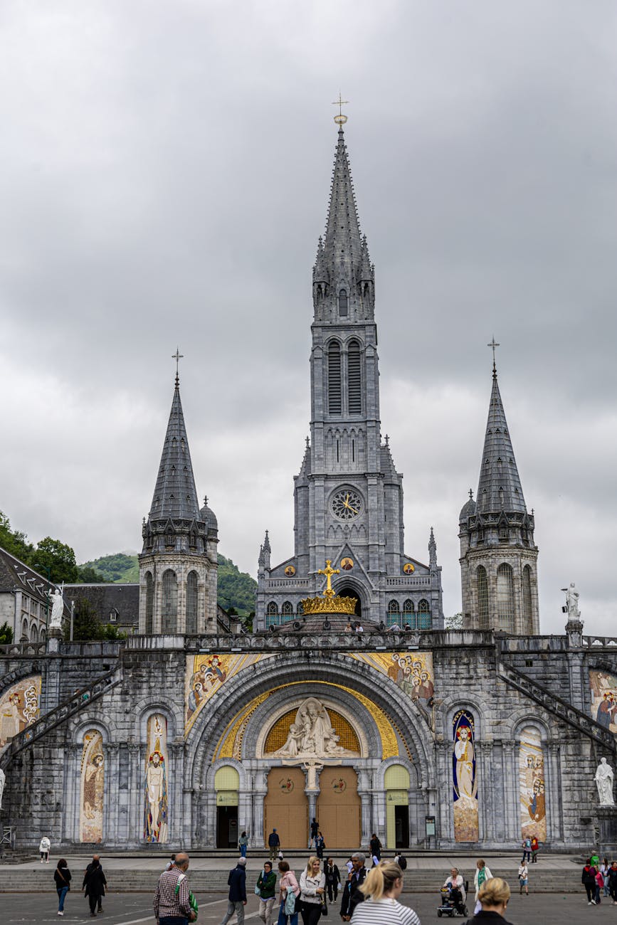 Basilique de Lourdes avec visiteurs sous un ciel nuageux