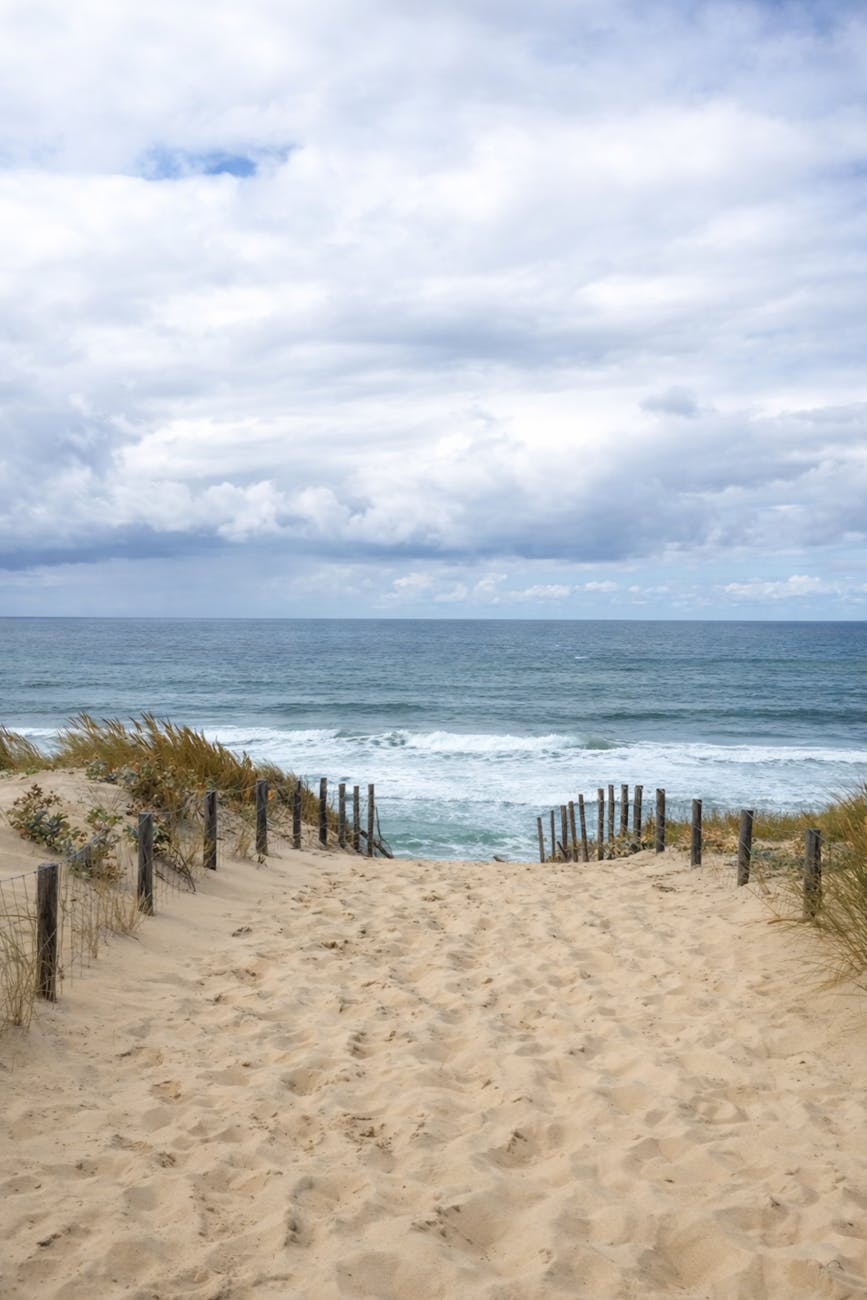 Plage de sable bordée d'un chemin sous un ciel nuageux