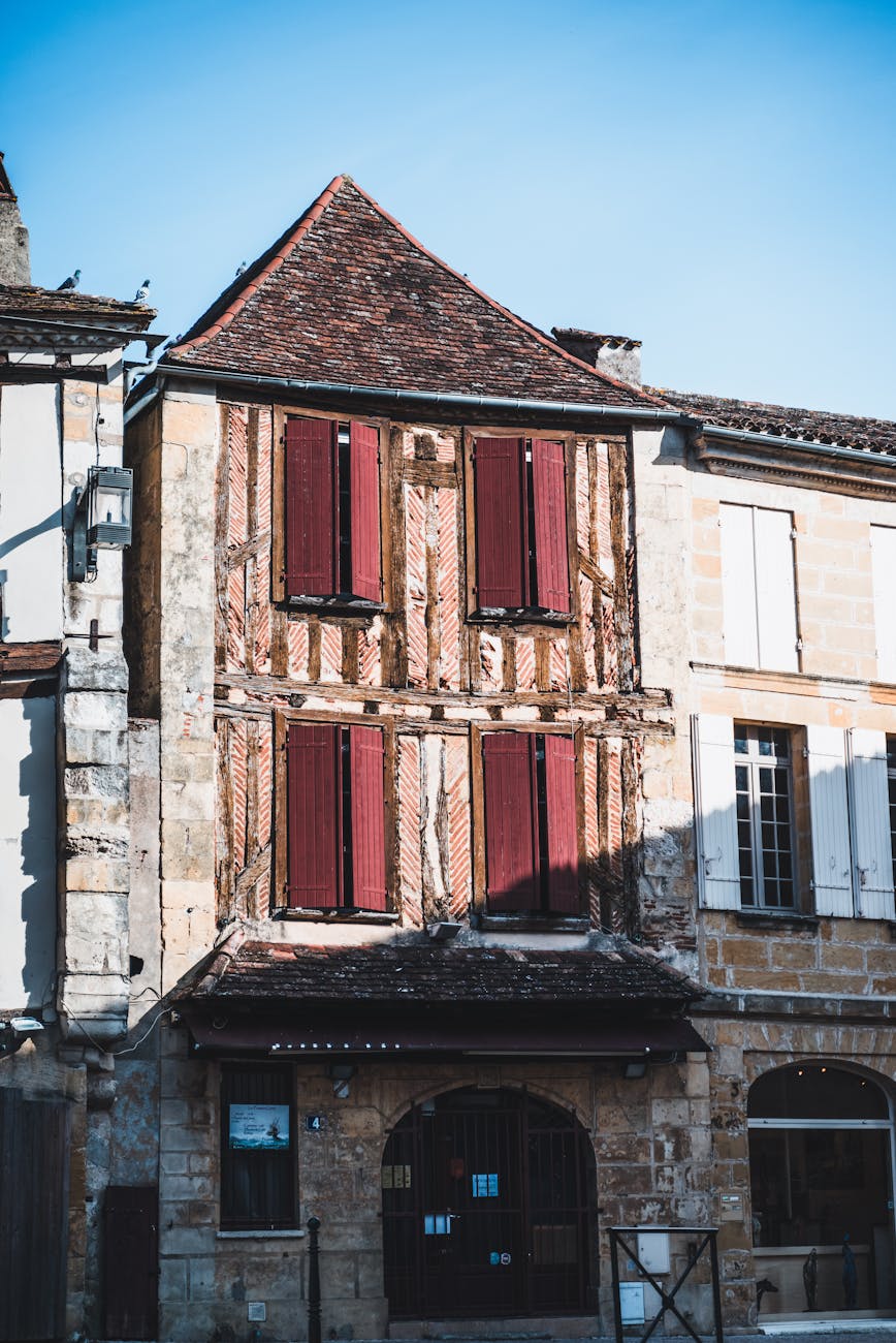 Maison à colombages avec volets rouges sur place de village