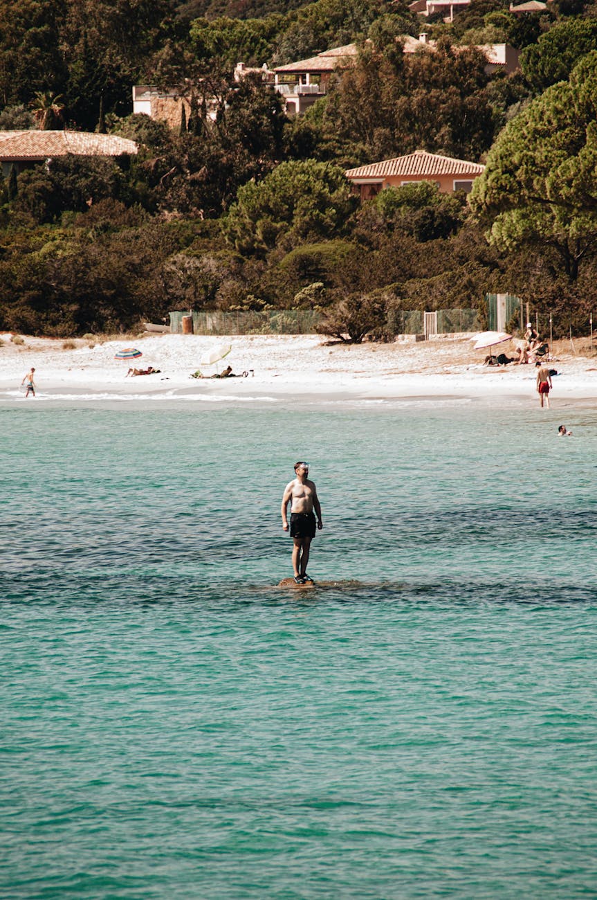 Homme en eaux peu profondes sur une plage corse au décor rocheux