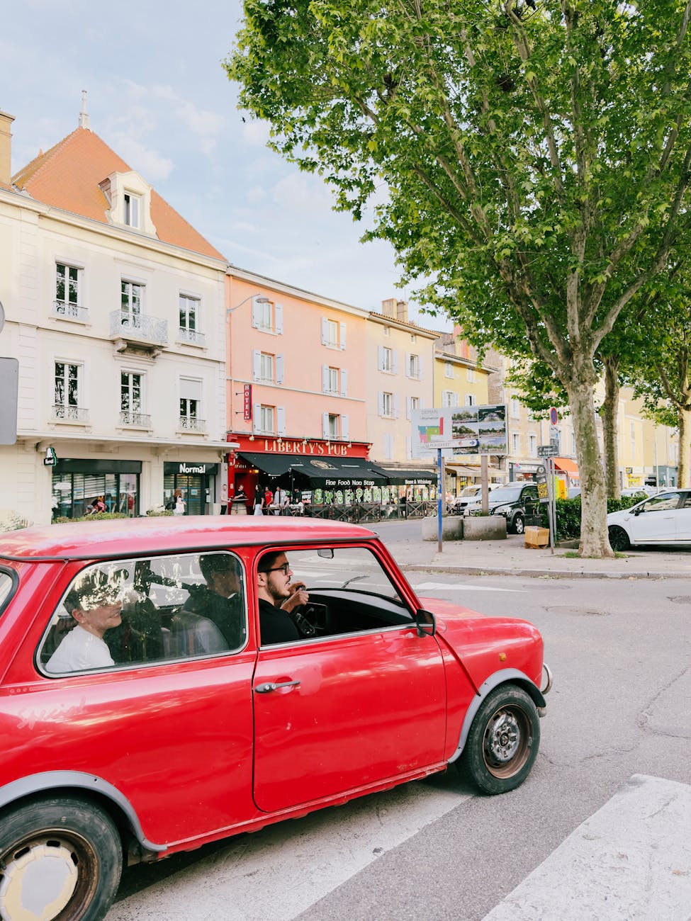 Voiture rouge dans une place de ville française avec maisons colorées