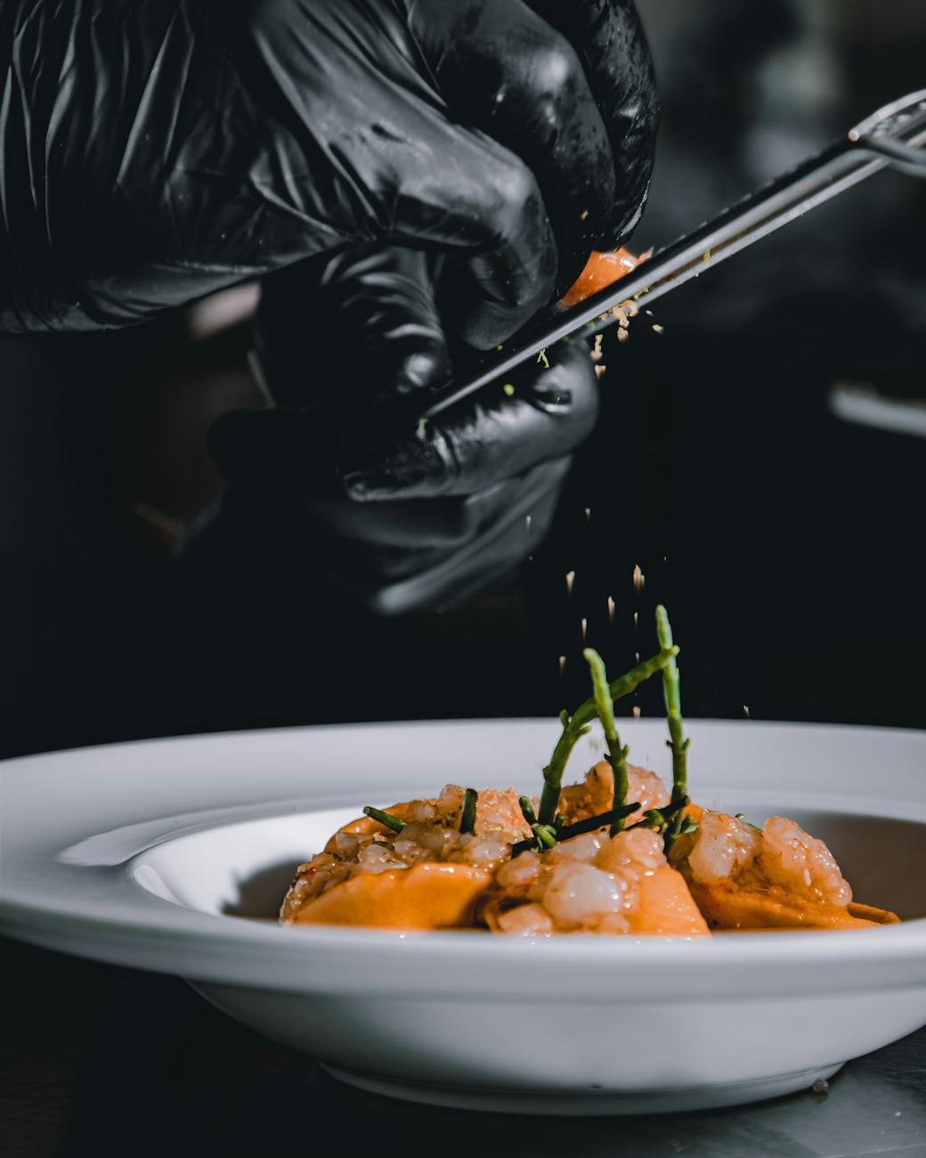 Mains gantées d'un chef assaisonnant un plat de fruits de mer