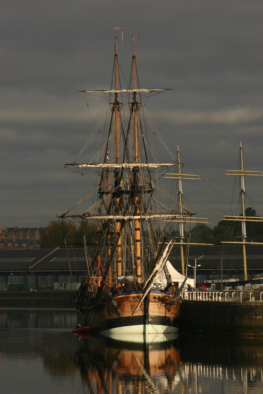 Trois-mâts historique amarré dans un port avec reflets sur l'eau calme sous un ciel dramatique