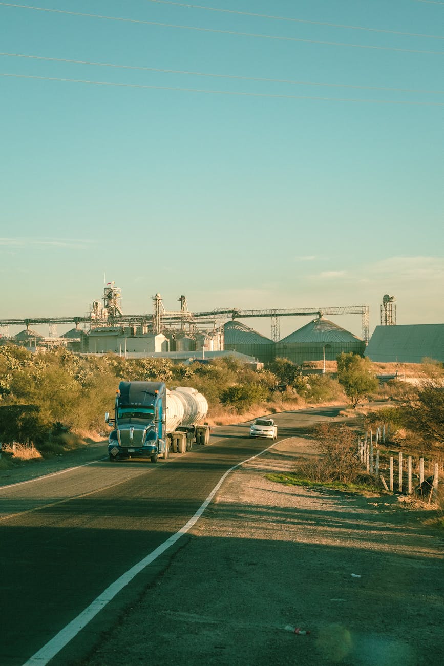 Semi-remorque bleu sur une route rurale longeant un complexe industriel