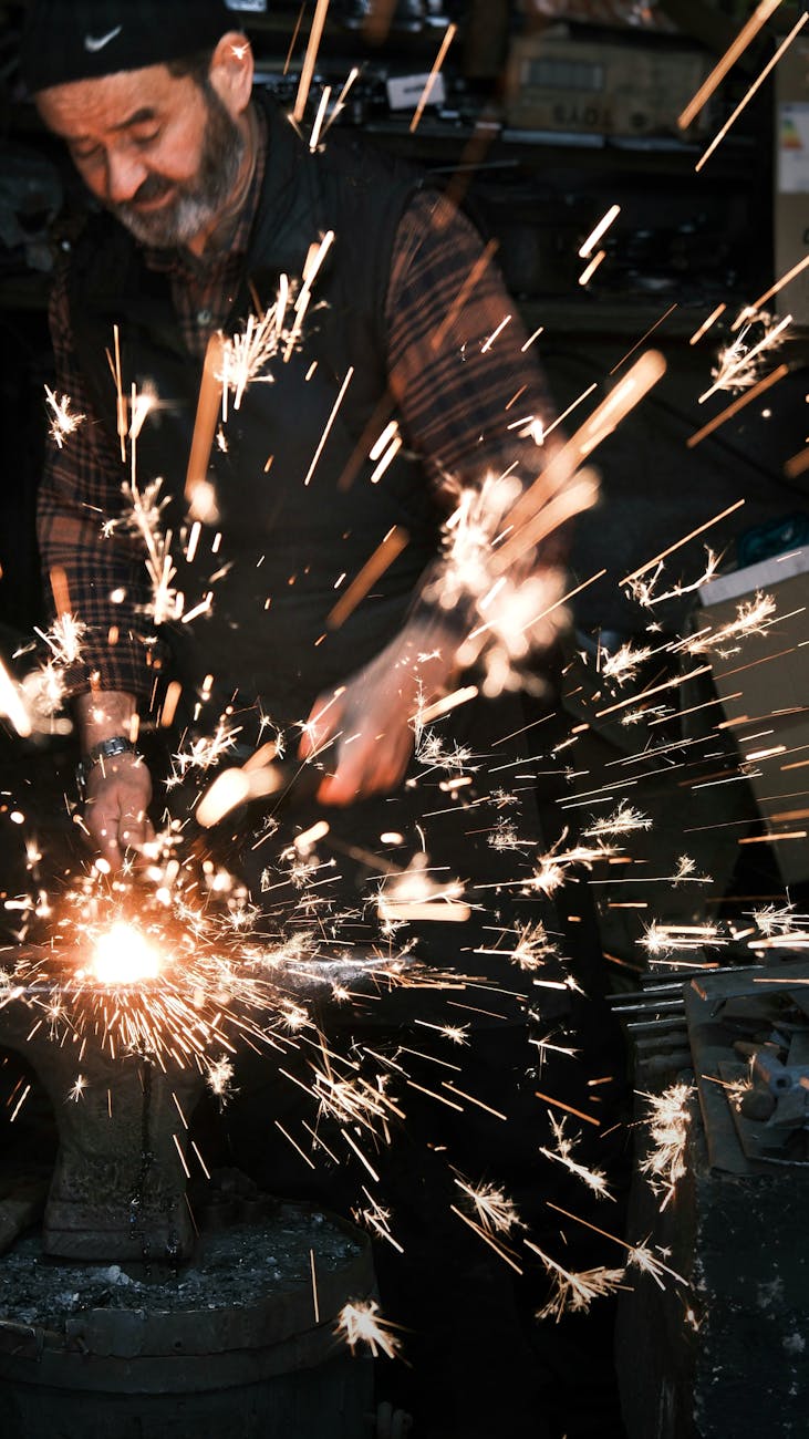 Adulte travaillant avec du métal, créant des étincelles brillantes dans un atelier industriel