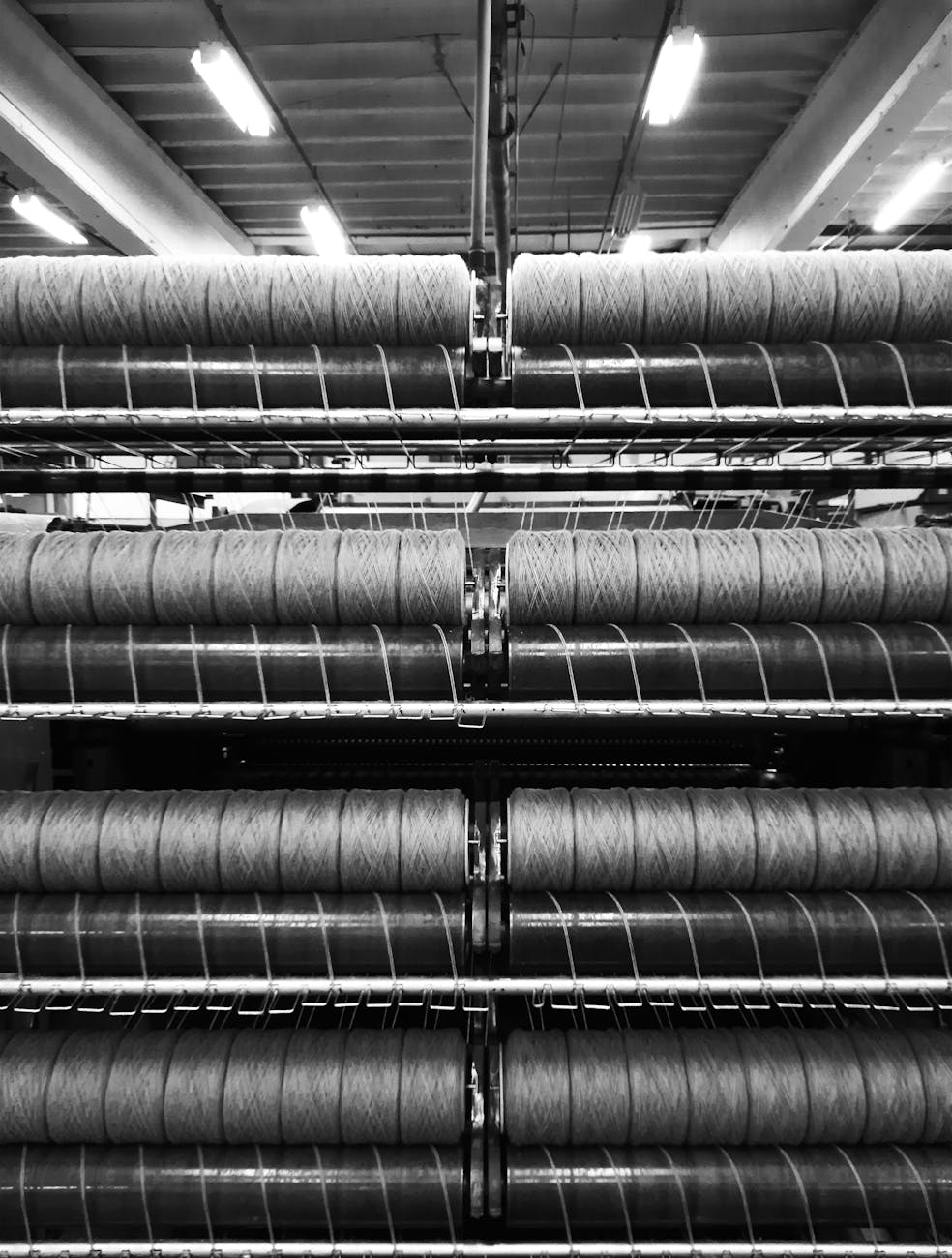 Image en noir et blanc montrant des rouleaux de fils empilés dans une usine textile