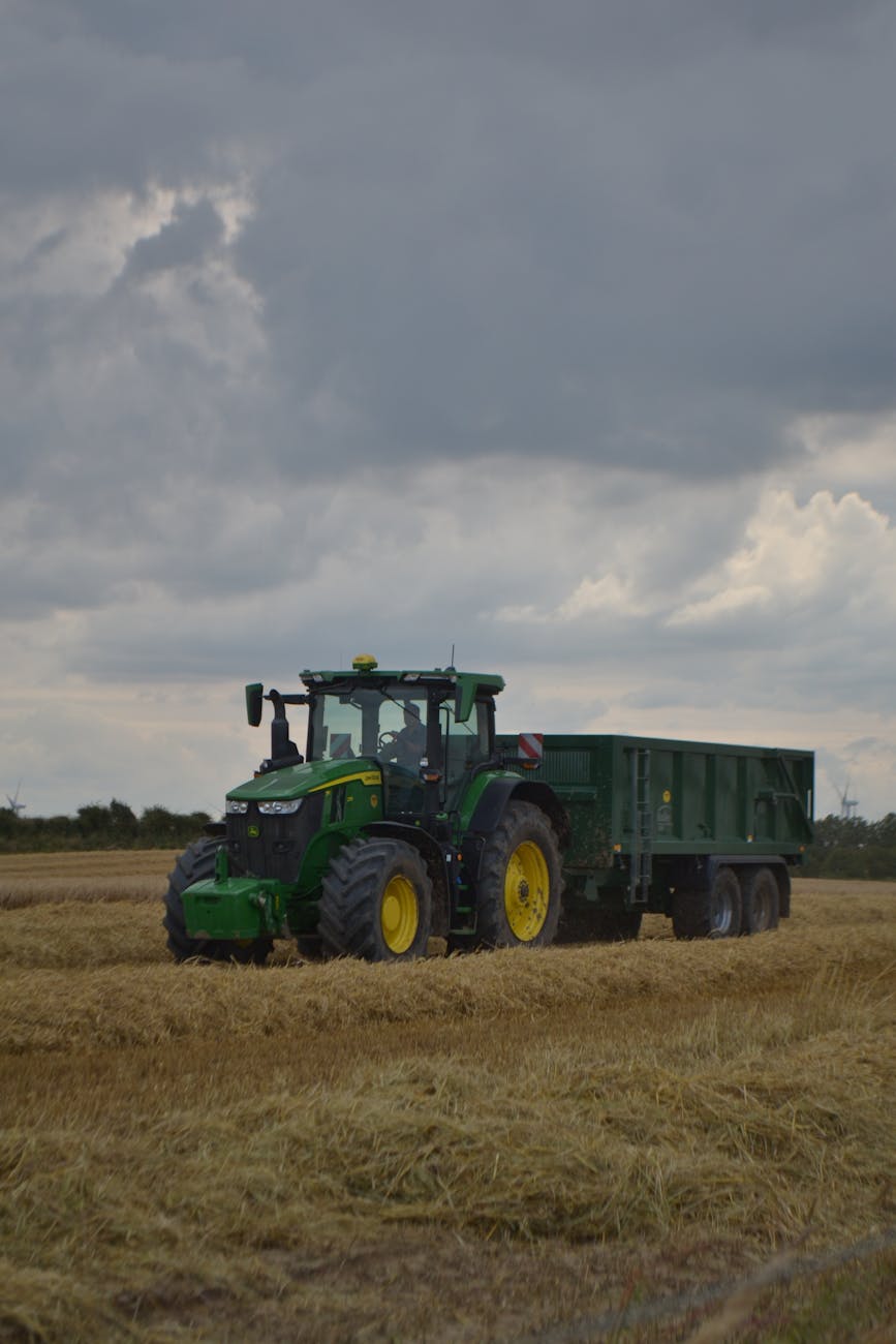 Tracteur vert tirant une remorque dans un champ de blé sous un ciel nuageux